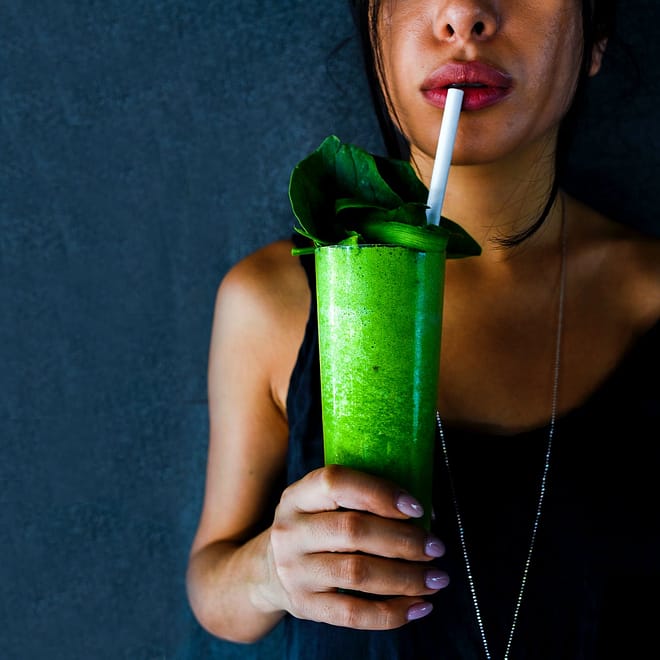 woman in black tank top holding a green smoothie